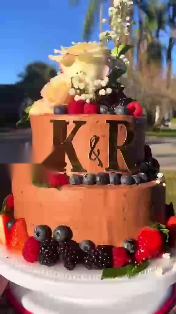 Two-tier terracotta wedding-style cake with fresh berries and florals, monogram lettering