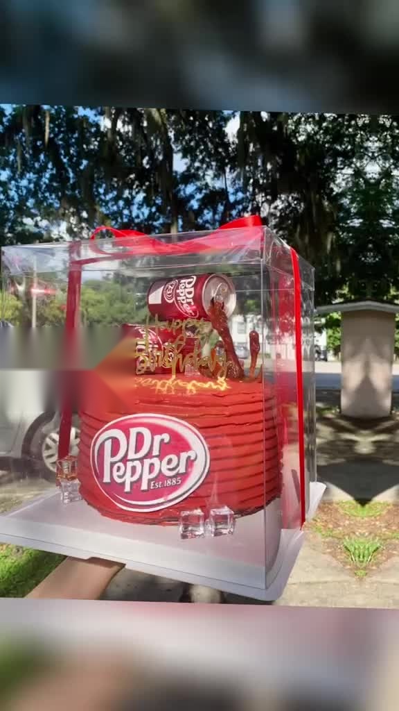 Dr Pepper themed birthday cake in a clear acrylic display box with red bow