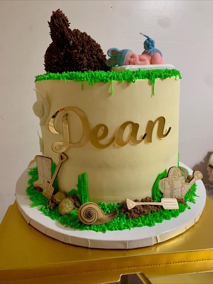 Garden-themed first birthday cake with buttercream grass, garden tool toppers, and a sleeping baby fondant figure