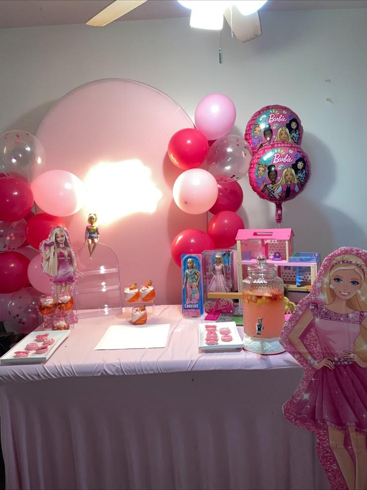 Pink Barbie-themed birthday dessert table with balloon arch, backdrop, and treats